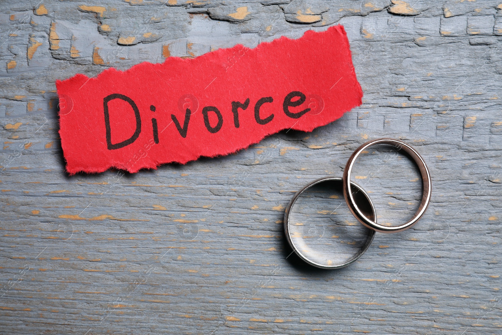 Photo of Paper sheet with word Divorce and wedding rings on grey wooden table, flat lay