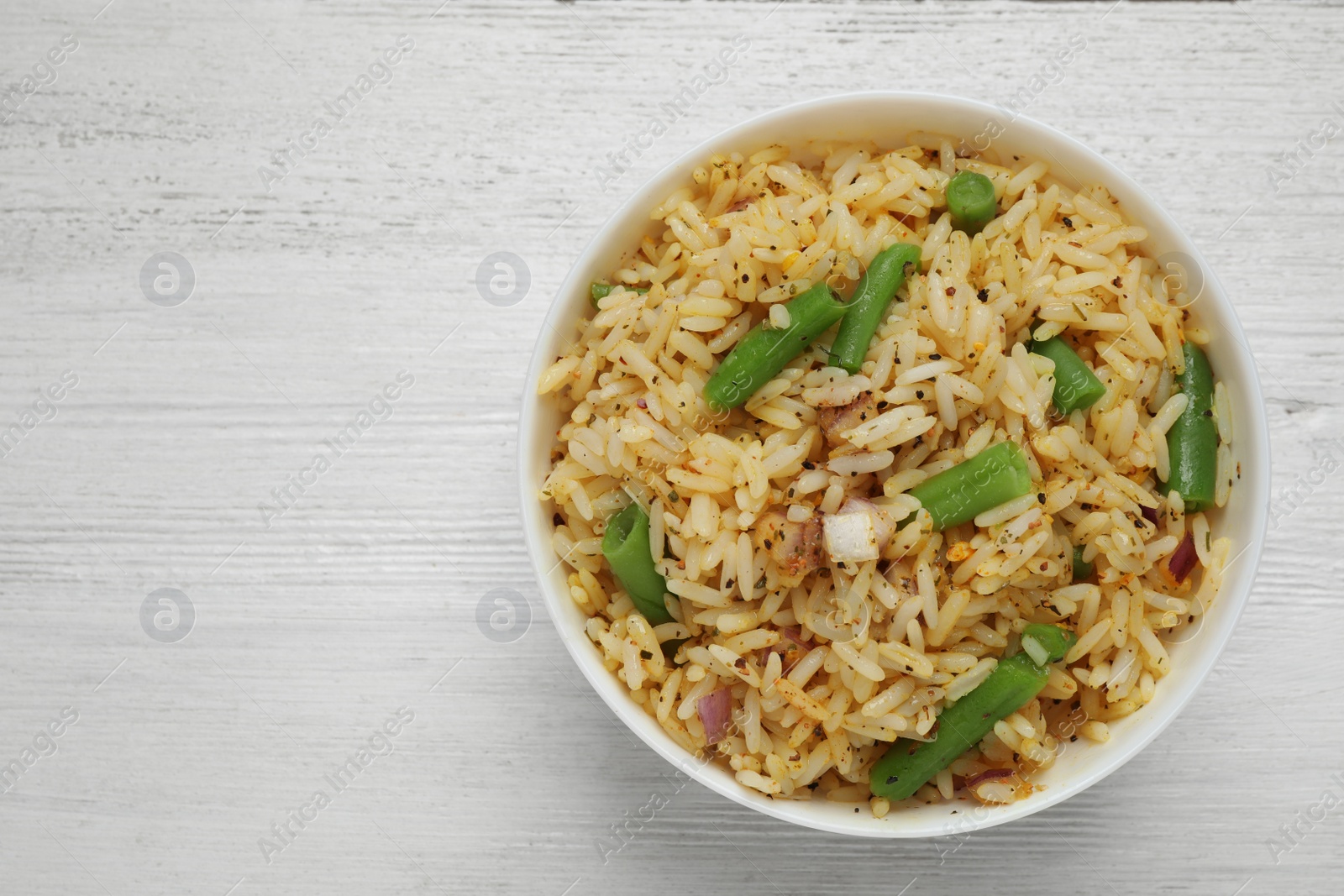 Photo of Tasty rice pilaf with vegetables on white wooden table, top view. Space for text