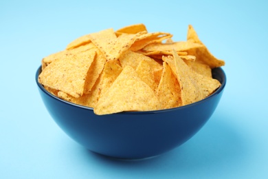 Photo of Bowl of tasty Mexican nachos chips on light blue background