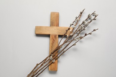 Photo of Wooden cross and willow branches on light grey background, top view. Easter attributes