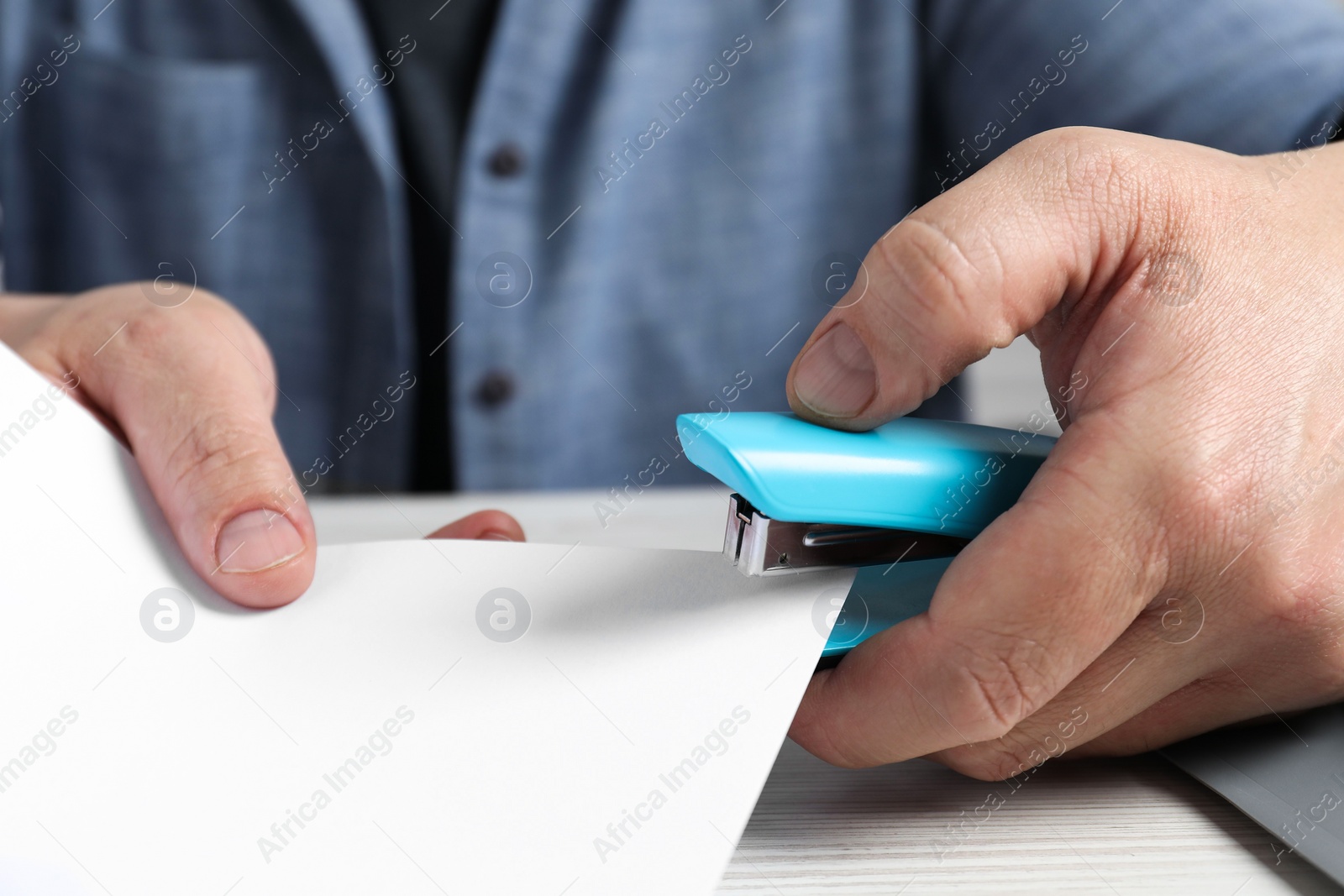 Photo of Man with papers using stapler at white table, closeup