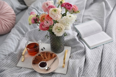 Photo of Bouquet of beautiful ranunculuses, croissant and tea on bed indoors