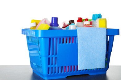 Shopping basket with different detergents and rag on grey table against white background