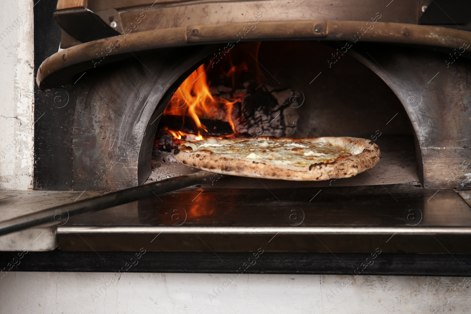 Photo of Oven with burning firewood and tasty pizza in restaurant kitchen