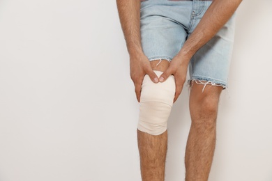 Man with bandage on his knee against light background, closeup. Space for text