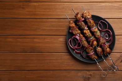 Photo of Metal skewers with delicious meat and onion served on wooden table, top view. Space for text