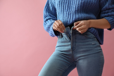 Photo of Woman unbuttoning jeans on pink background, closeup