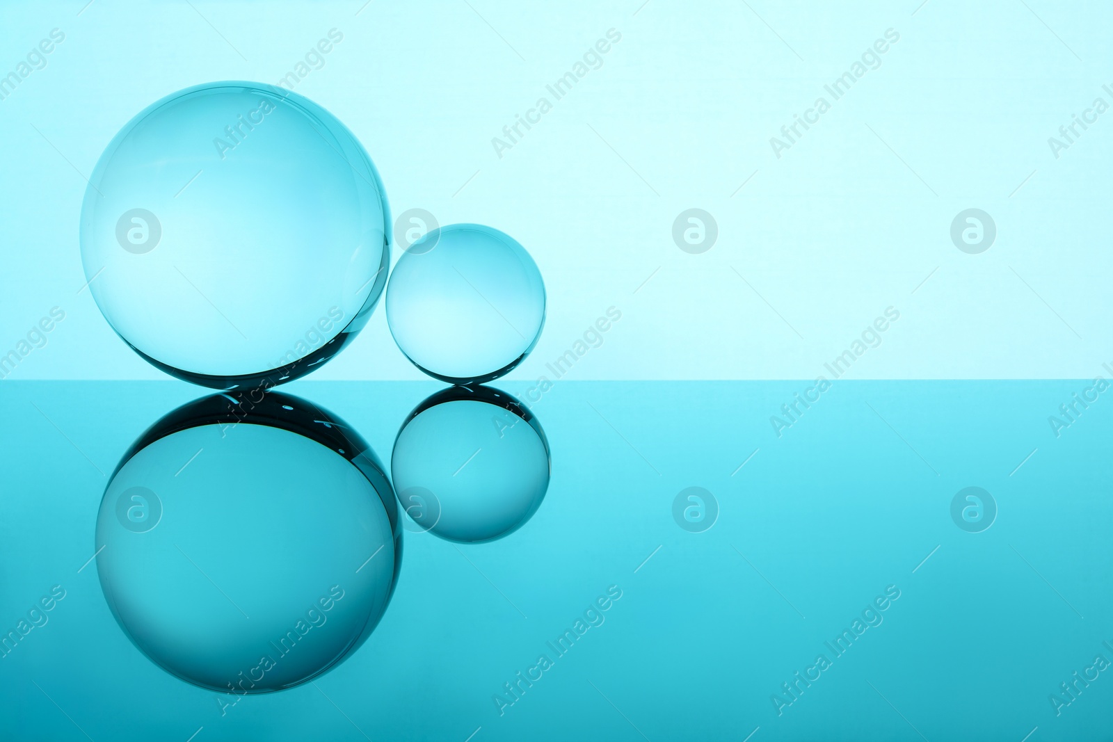 Photo of Transparent glass balls on mirror surface against turquoise background. Space for text