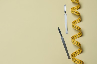 Scalpels and measuring tape on beige background, flat lay with space for text. Weight loss surgery