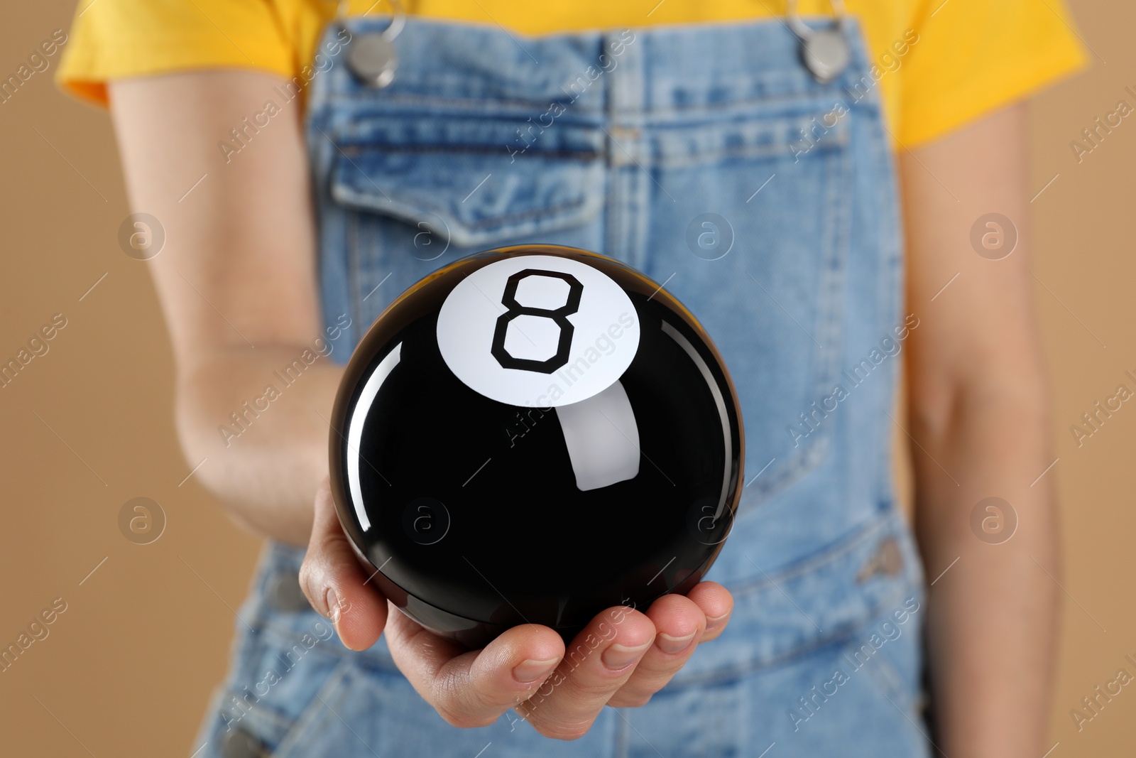 Photo of Woman holding magic eight ball on light brown background, closeup