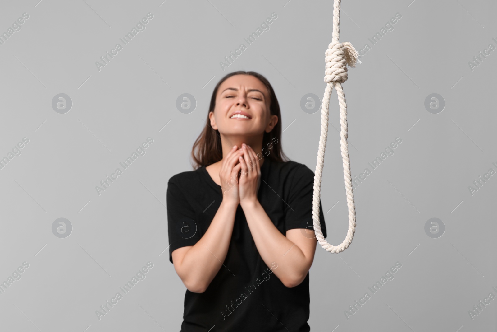Photo of Depressed woman crying near rope noose on light grey background