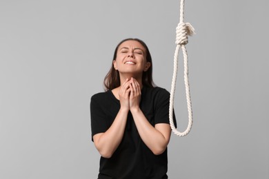 Depressed woman crying near rope noose on light grey background