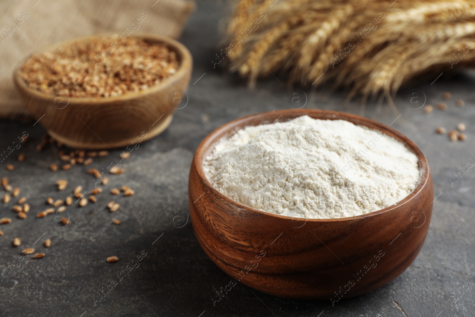 Photo of Wooden bowl of flour on grey table. Space for text