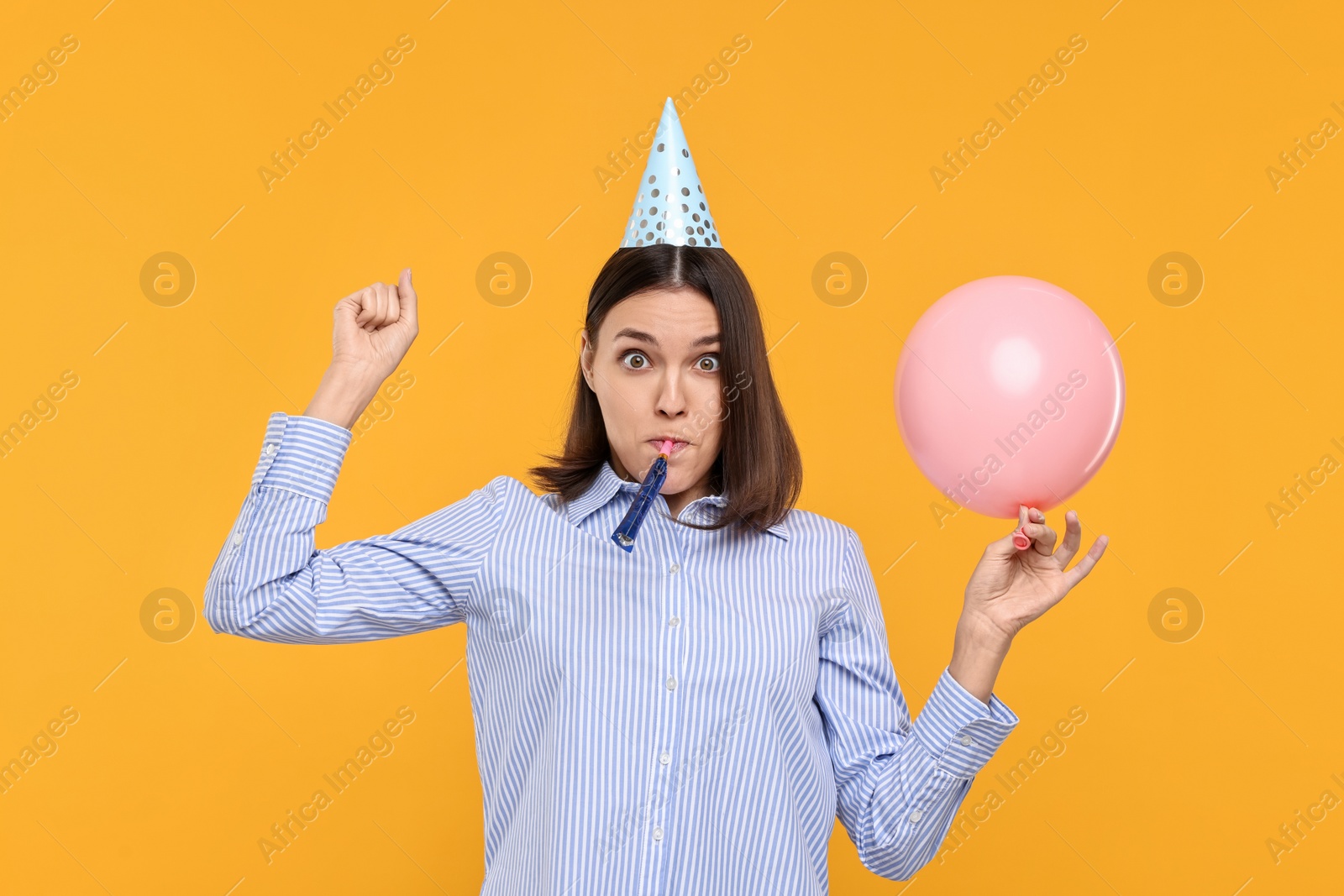 Photo of Young woman in party hat with balloon and blower on yellow background