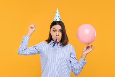 Photo of Young woman in party hat with balloon and blower on yellow background