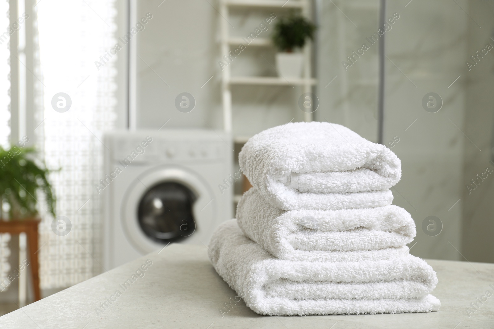 Photo of Stack of clean towels on table in laundry room. Space for text