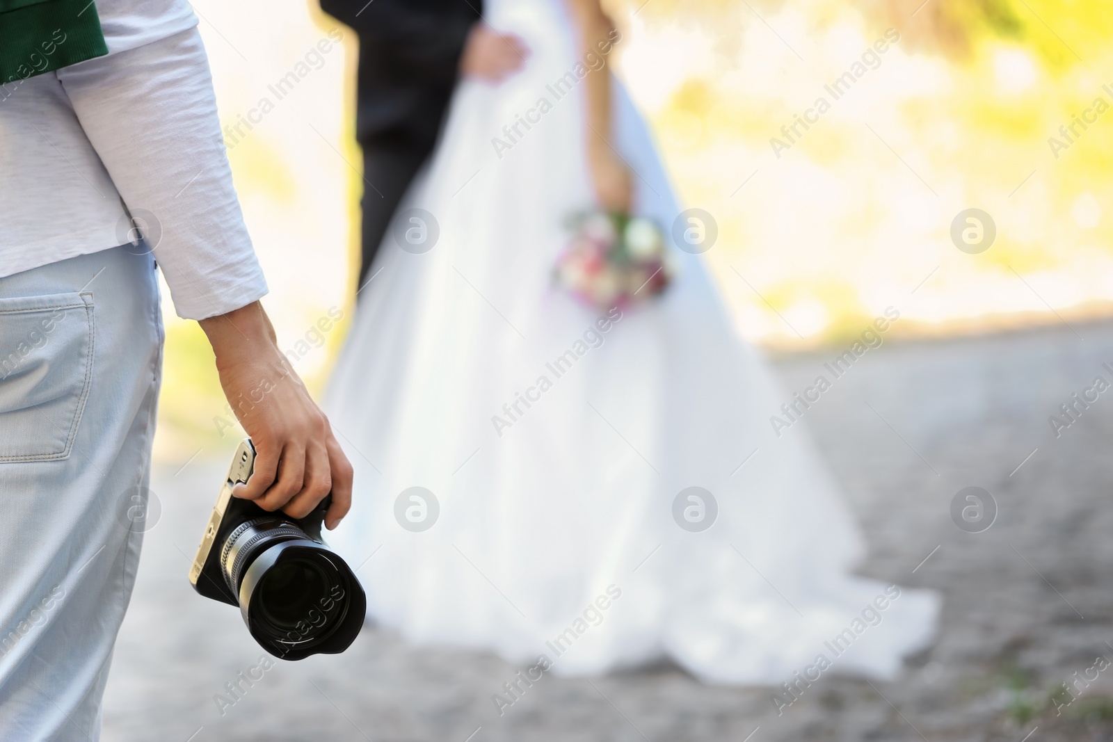 Photo of Professional photographer with camera and wedding couple, outdoors