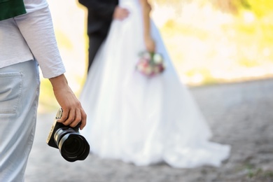 Photo of Professional photographer with camera and wedding couple, outdoors