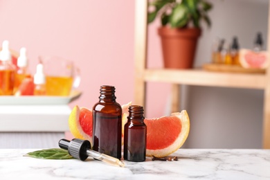 Bottles of essential oil and grapefruit slices on table against blurred background. Space for text