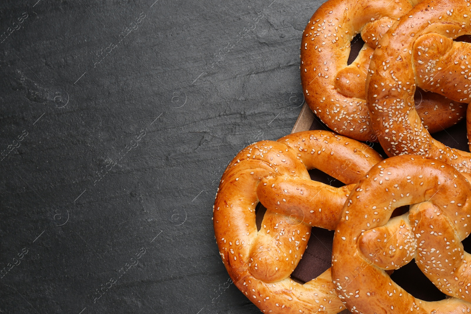 Photo of Delicious pretzels with sesame seeds on black table, top view. Space for text