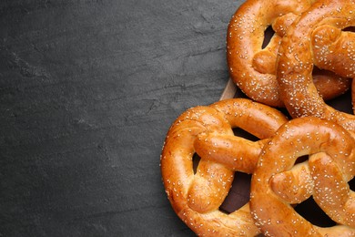 Photo of Delicious pretzels with sesame seeds on black table, top view. Space for text