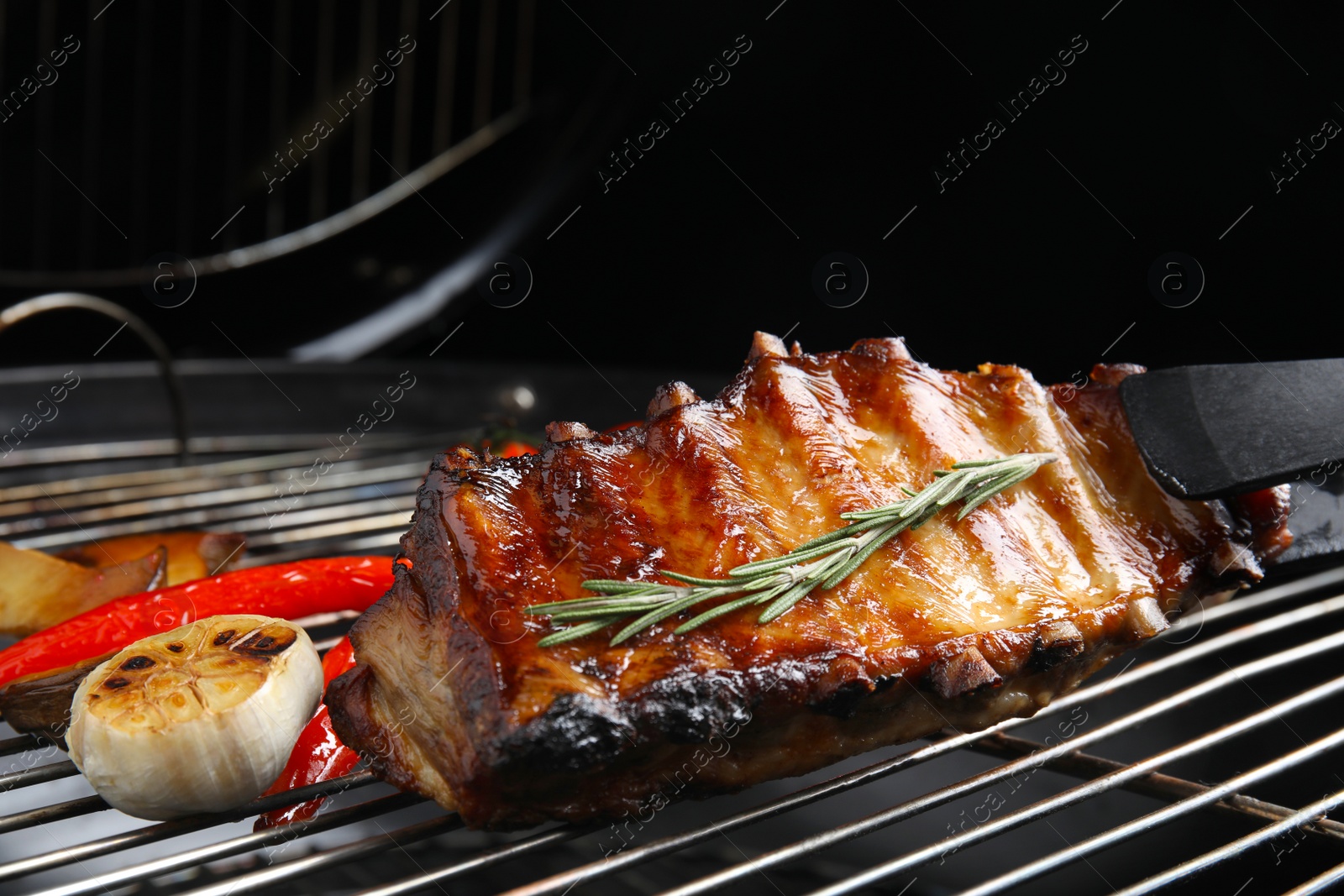 Photo of Delicious ribs with rosemary and vegetables on barbecue grill