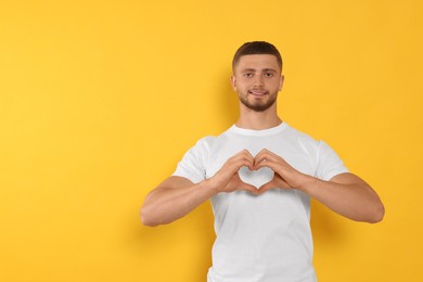 Photo of Happy volunteer making heart with his hands on orange background. Space for text