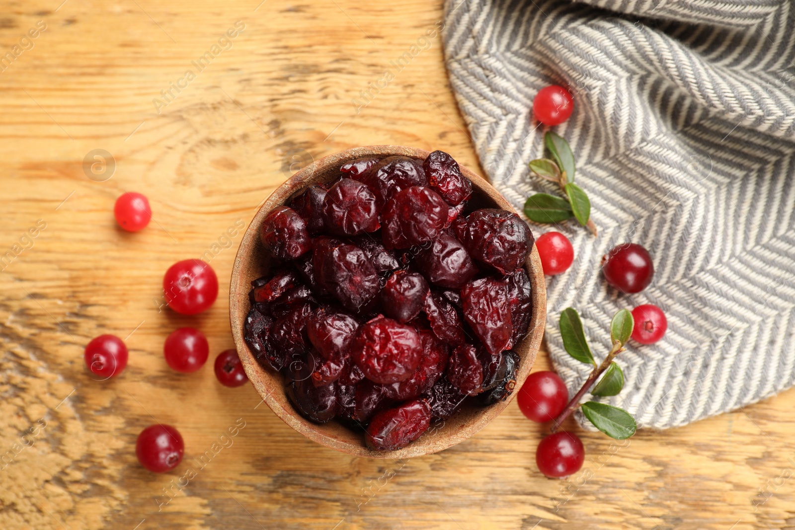 Photo of Tasty dried cranberries in bowl, fresh ones and leaves on wooden table, top view
