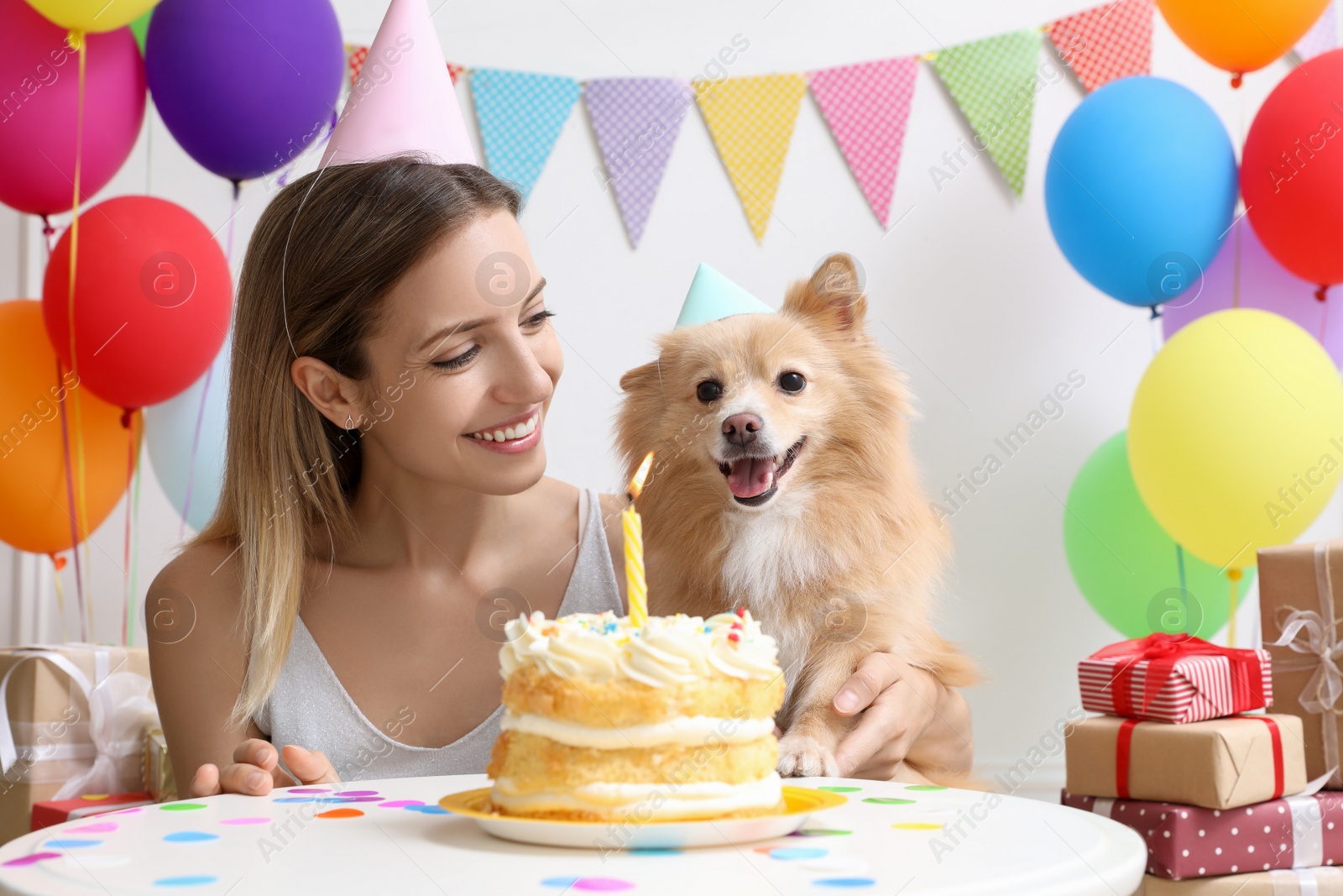 Photo of Happy woman celebrating her pet's birthday in decorated room