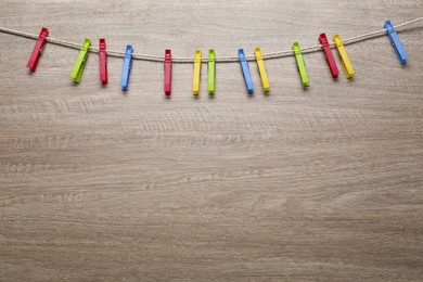 Photo of Colorful plastic clothespins and rope on wooden background. Space for text