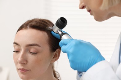 Trichologist with dermatoscope examining patient`s hair in clinic, closeup