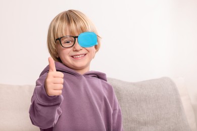 Photo of Happy boy with nozzle on glasses for treatment of strabismus showing thumbs up in room. Space for text