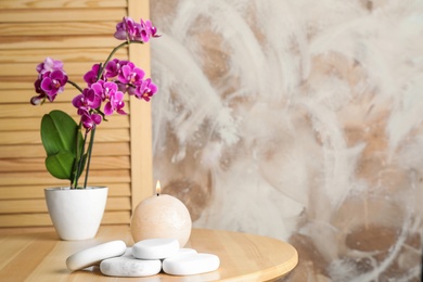 Photo of Spa stones, candle and blooming orchid indoors, space for text