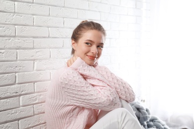 Young woman wearing knitted sweater near white brick wall