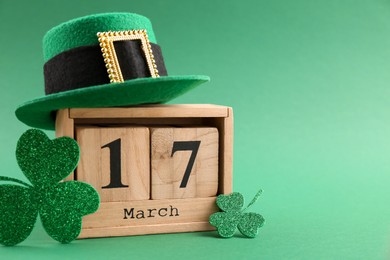 Photo of St. Patrick's day - 17th of March. Wooden block calendar, leprechaun hat and decorative clover leaves on green background. Space for text