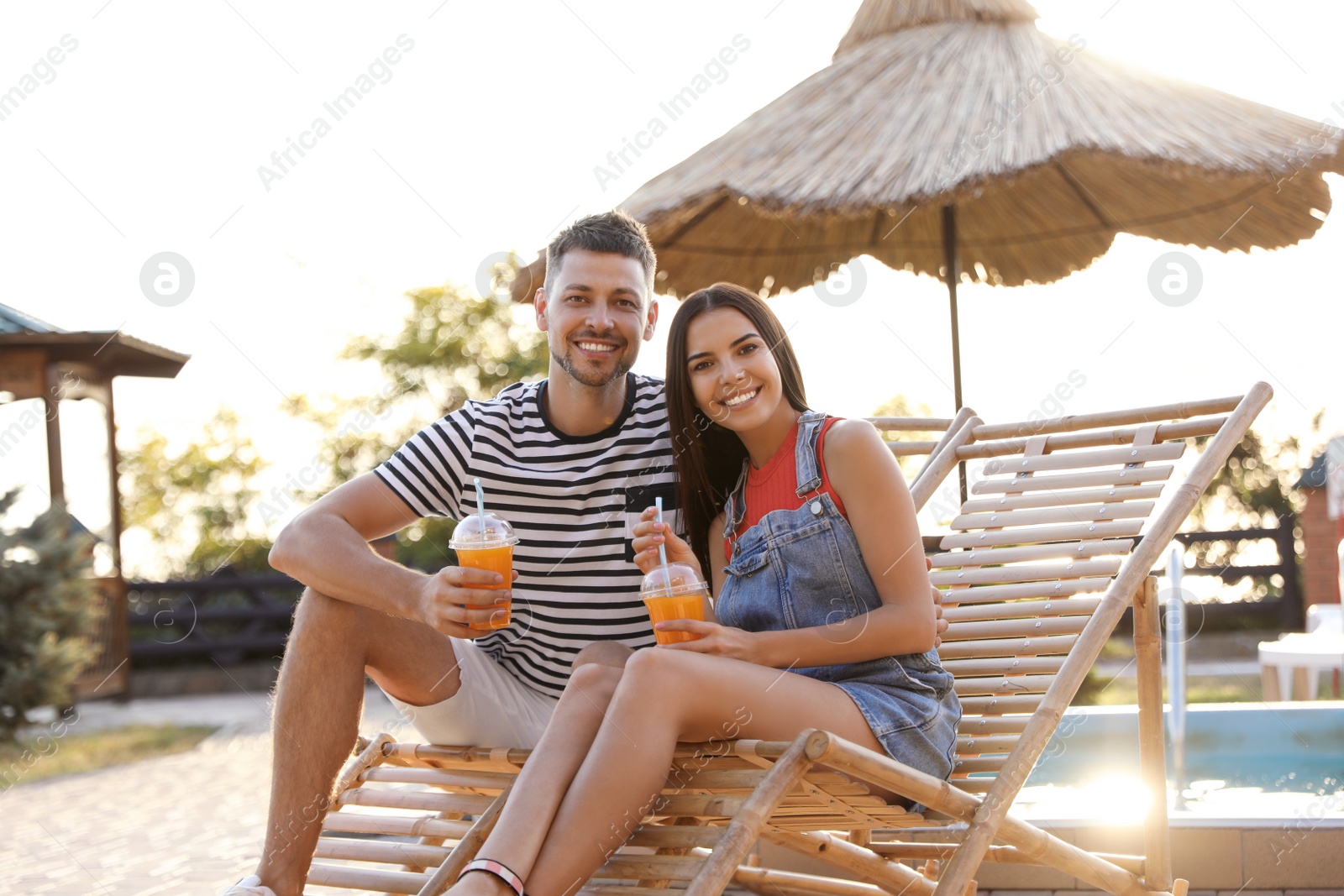 Image of Happy couple with cups of refreshing drink resting in deck chairs outdoors