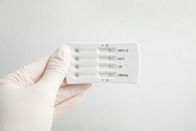 Photo of Doctor in gloves holding disposable express test for hepatitis on white background, closeup