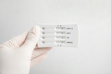 Doctor in gloves holding disposable express test for hepatitis on white background, closeup