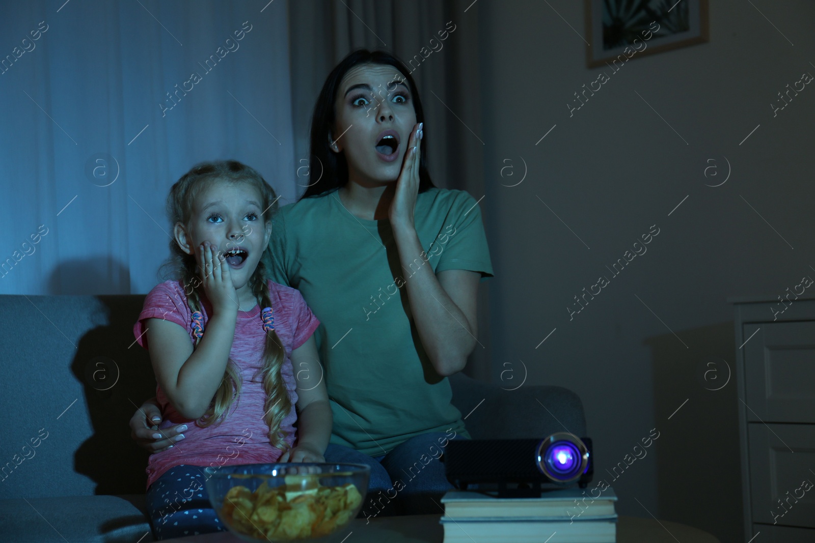 Photo of Emotional young woman and her daughter watching movie using video projector at home