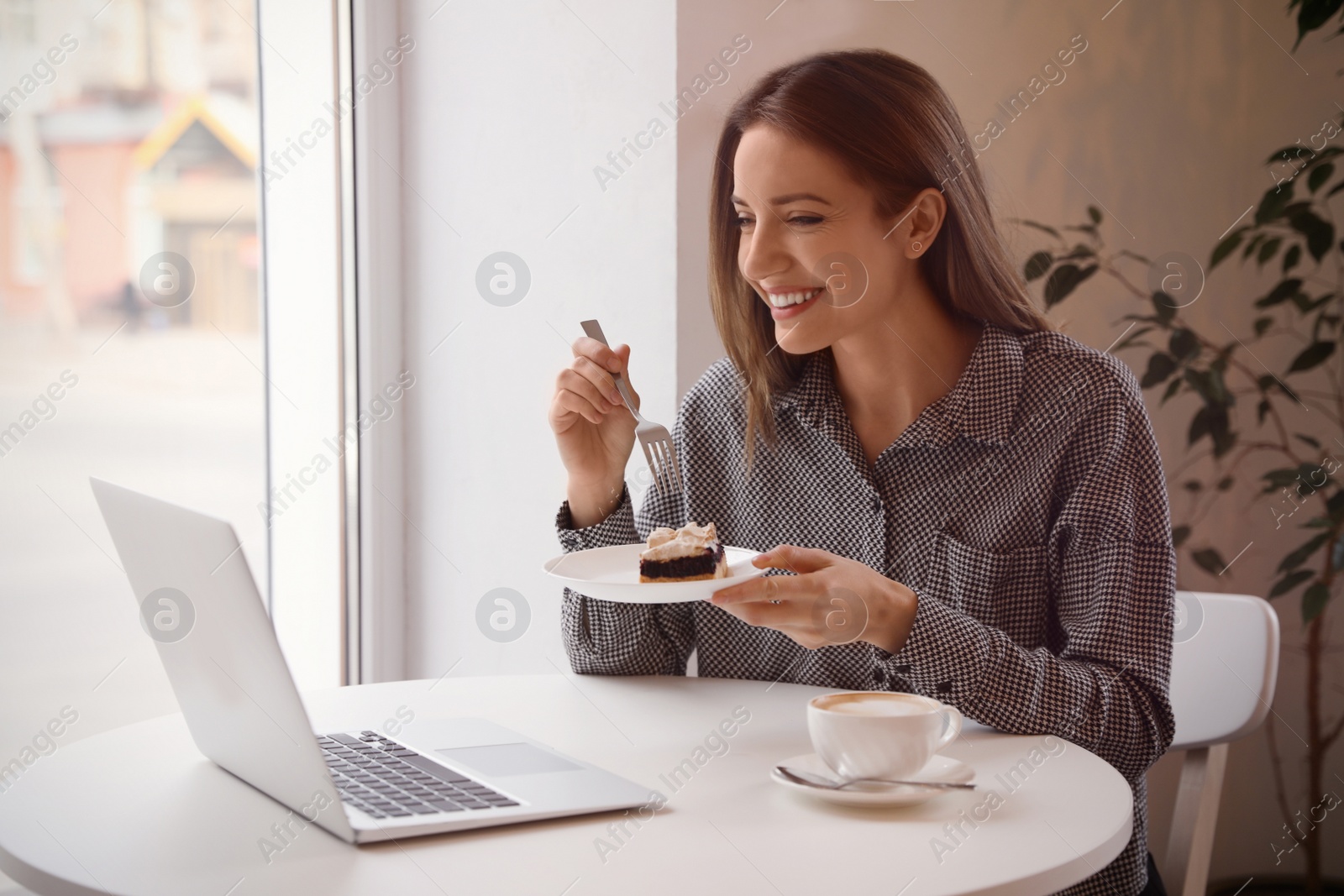 Photo of Young blogger with laptop eating dessert at table in cafe