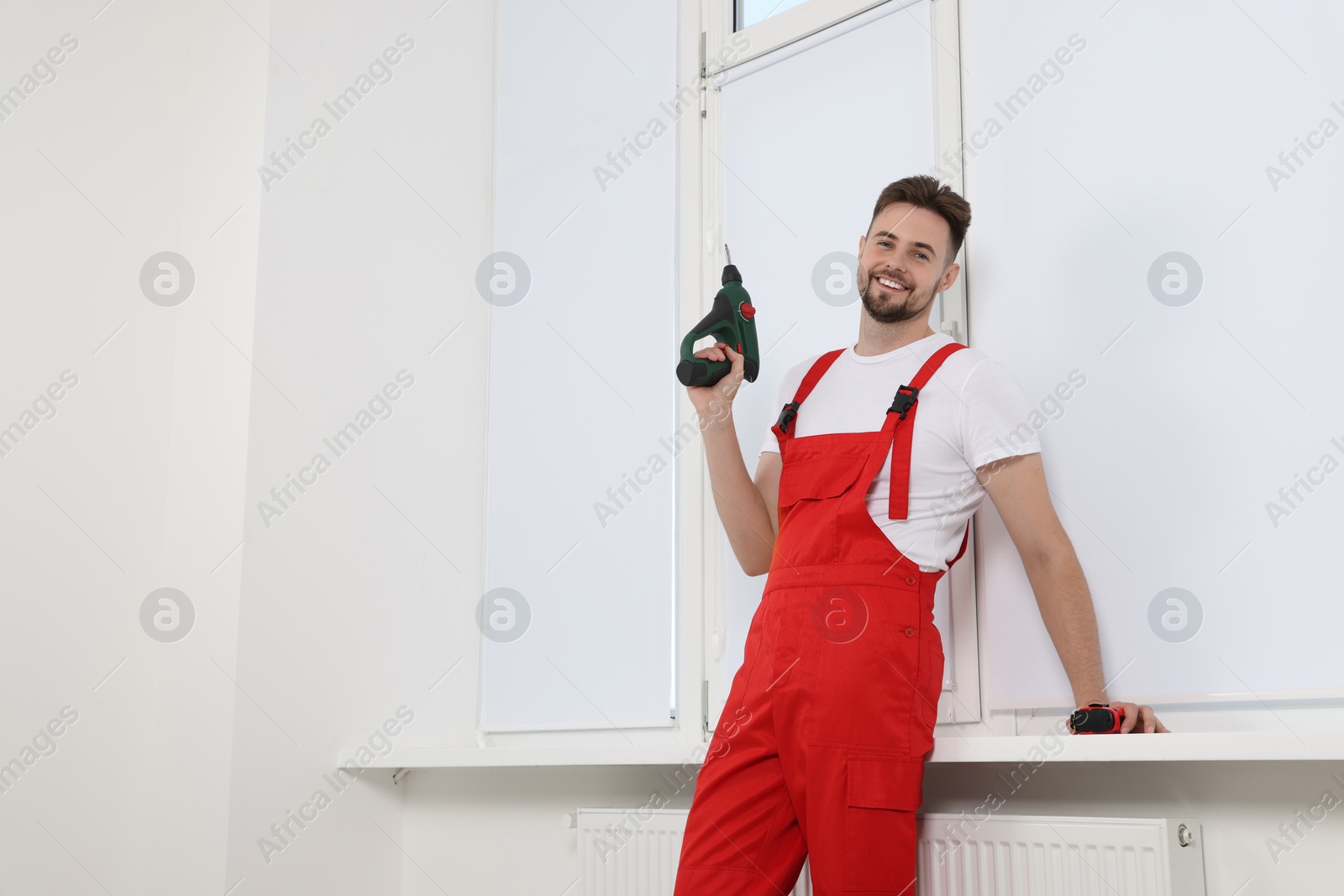 Photo of Worker holding tools for installation roller window blinds indoors