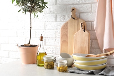 Fresh oil, olives and kitchen utensils on table near brick wall