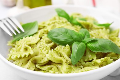 Delicious pasta with pesto sauce and basil in bowl, closeup