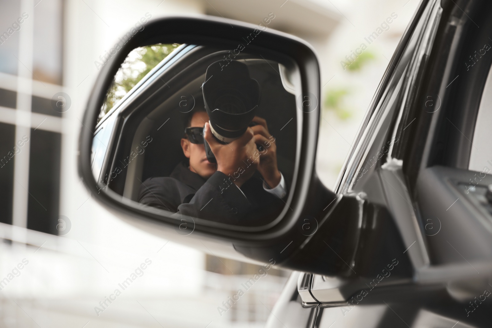 Photo of Private detective with camera spying from auto, view through car side mirror