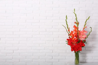 Photo of Vase with beautiful gladiolus flowers on table against white brick wall. Space for text