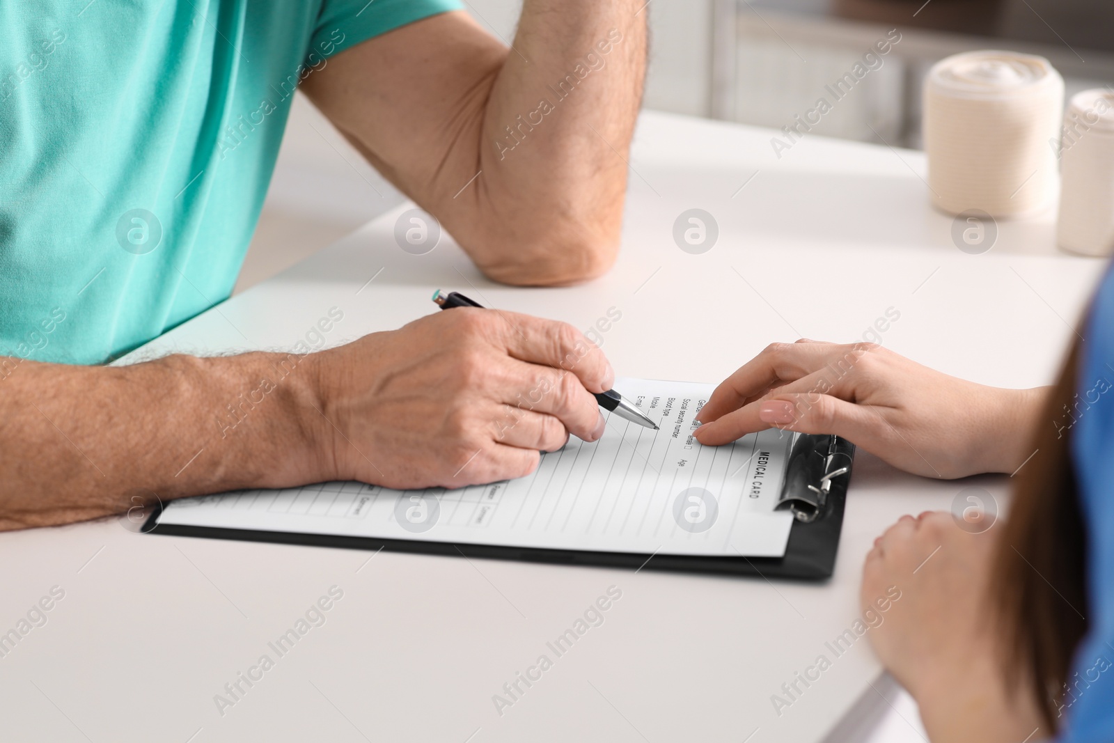 Photo of Doctor helping patient filling his medical card at table in clinic, closeup