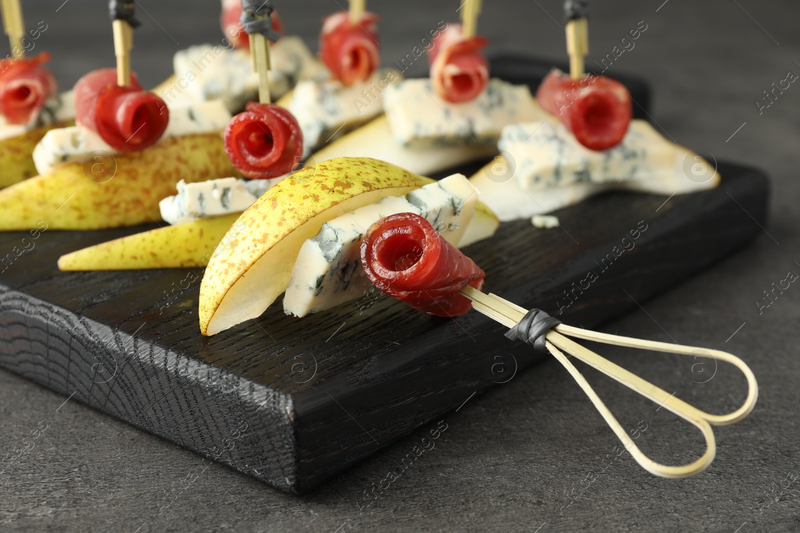 Photo of Tasty canapes with pears, blue cheese and prosciutto on grey table, closeup