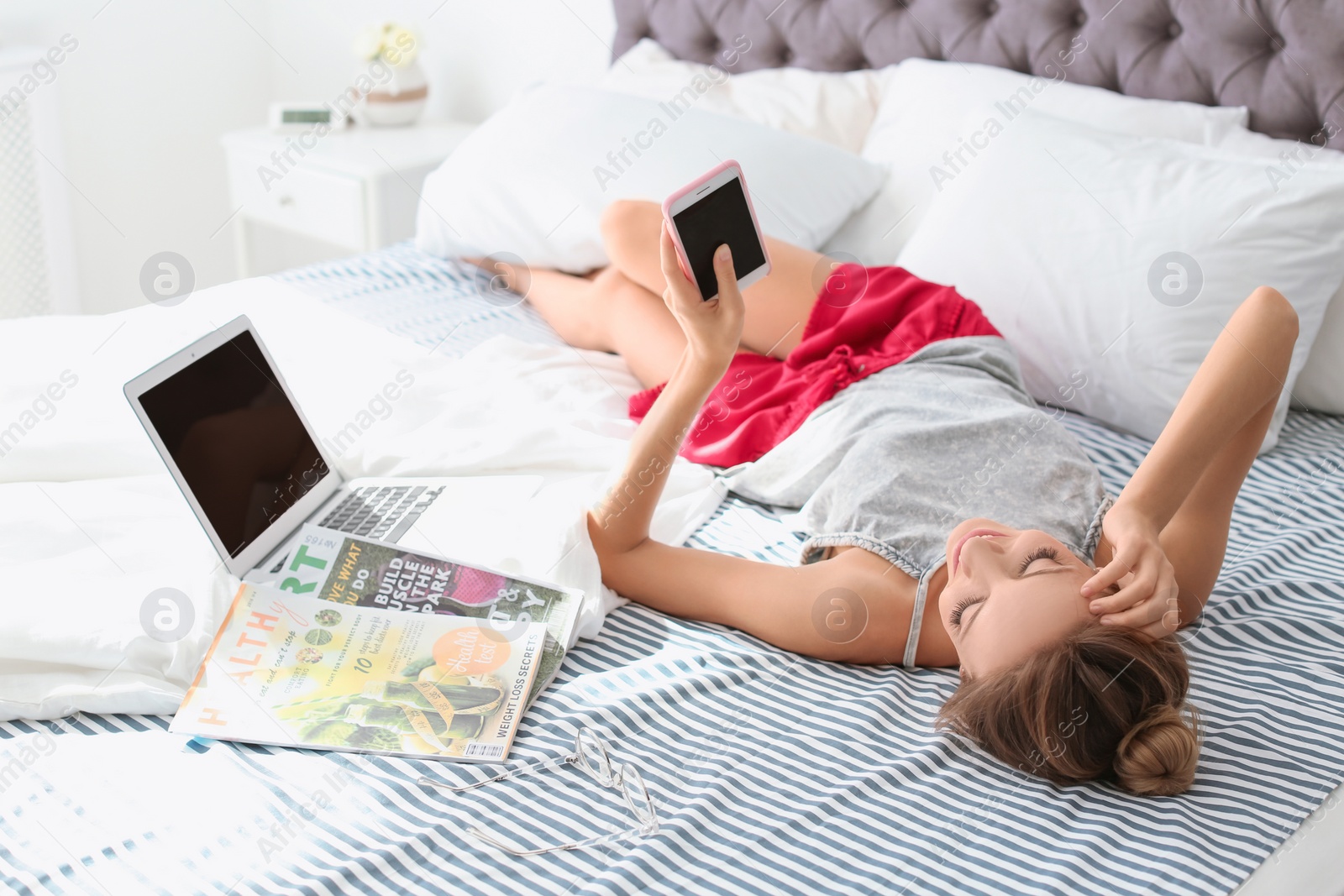 Photo of Beautiful young woman using smartphone in bed at home. Lazy morning