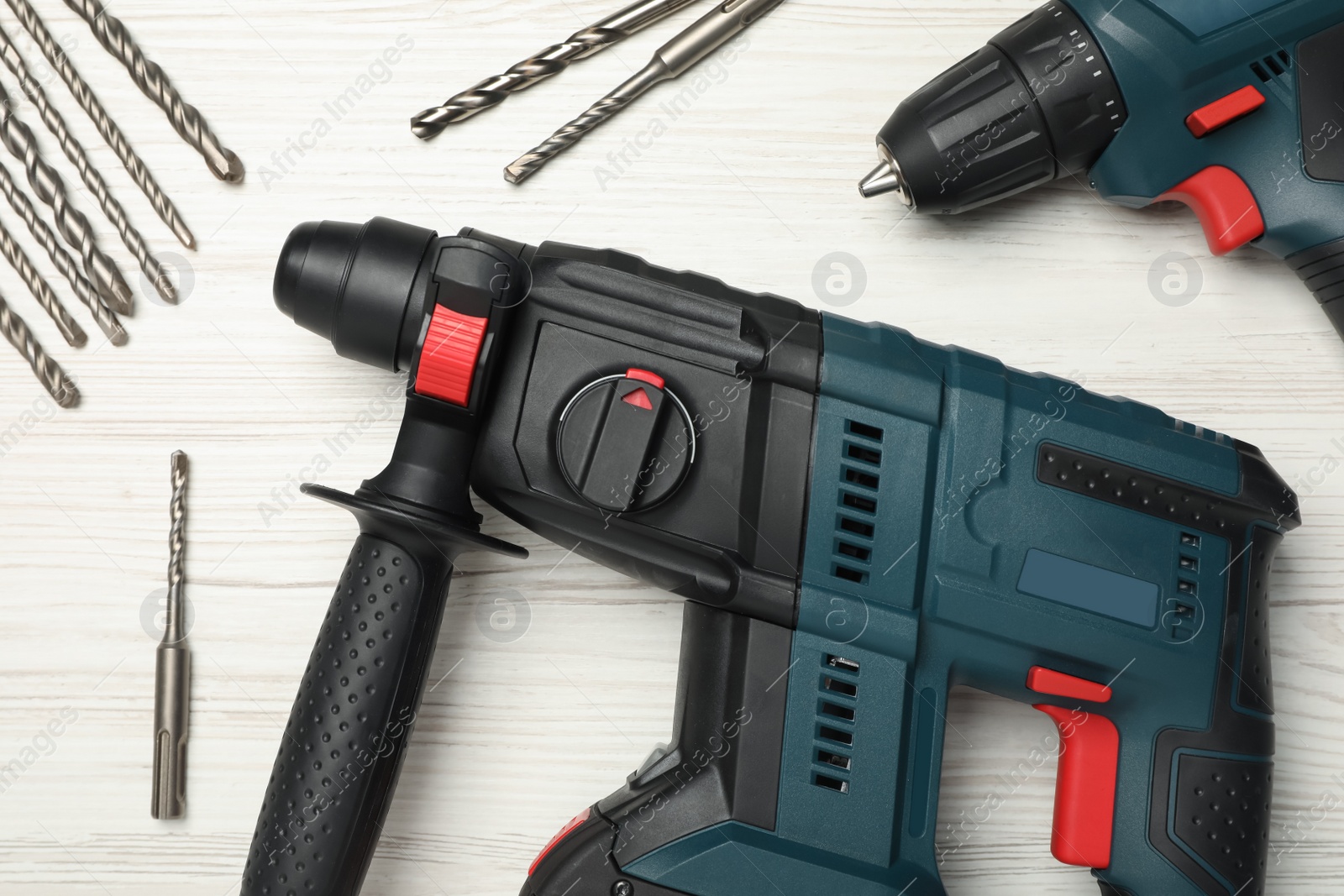 Photo of Modern electric power drills with twist bits on white wooden table, flat lay