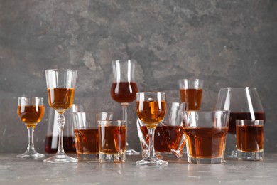 Photo of Different delicious liqueurs in glasses on grey table